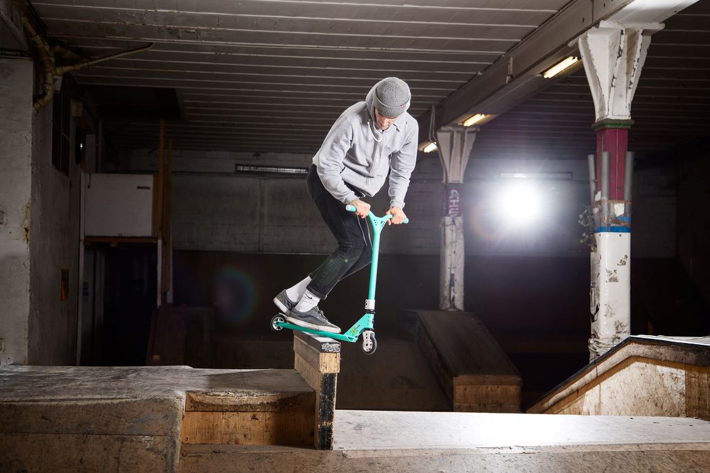 un homme réalisant une glisse sur une rampe, figure de trottinette freestyle